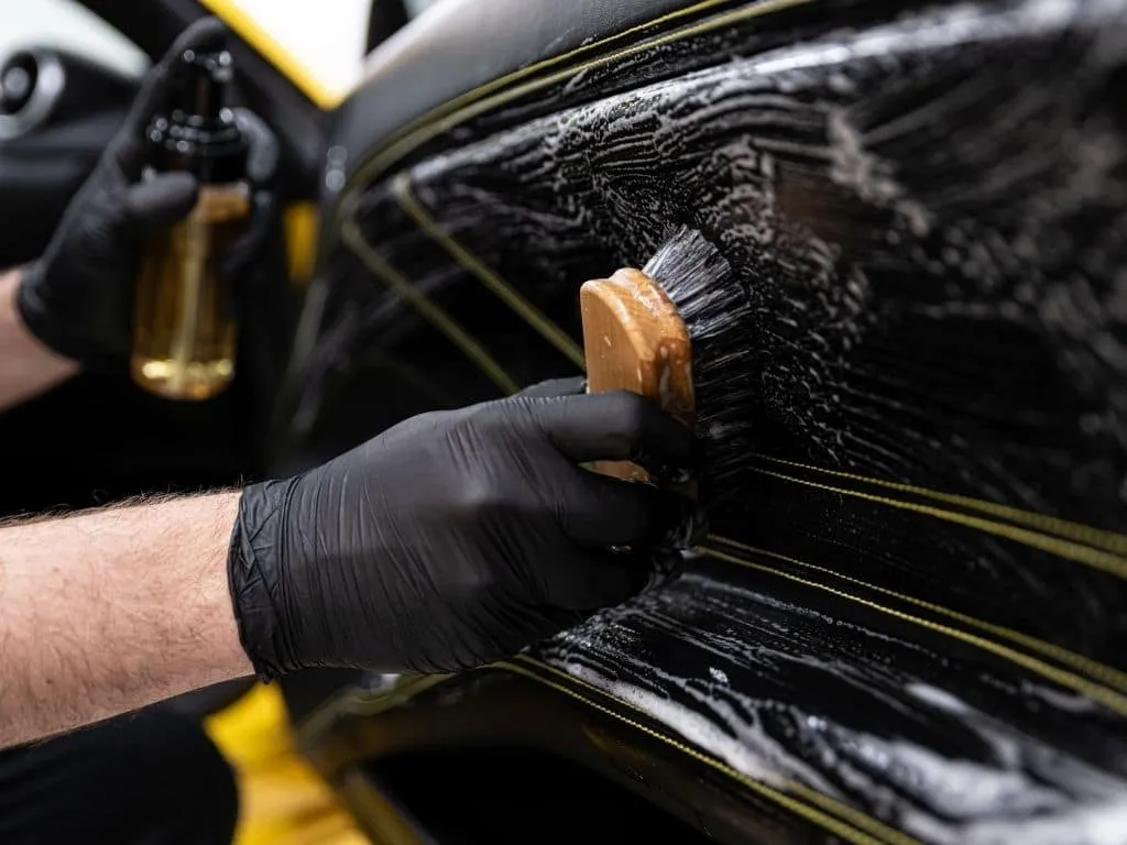 Car shampooing image showing a technician applying shampoo to the vehicle's interior seats for deep cleaning